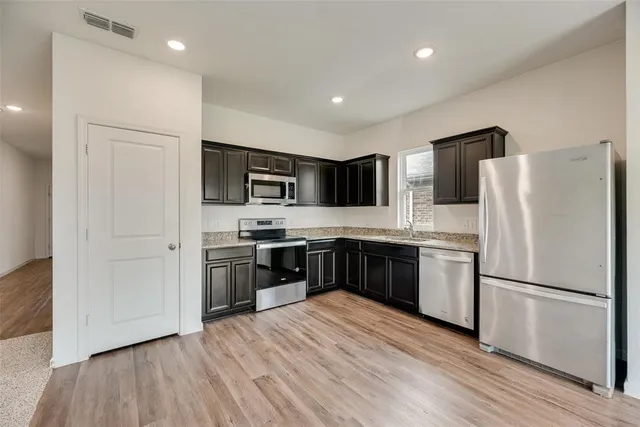 a kitchen with stainless steel appliances granite countertop a refrigerator stove a sink and a microwave with wooden floor