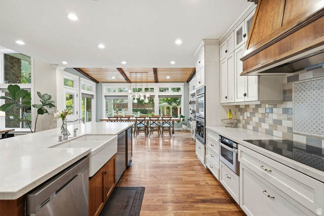 672 Perry Hollow Drive Mapleton, UT 84664 - Photo 28 of 106 Expansive kitchen featuring wood-finish flooring, a large island with a farmhouse sink, white perimeter cabinetry, stainless steel appliances, and a wood-paneled ceiling treatment