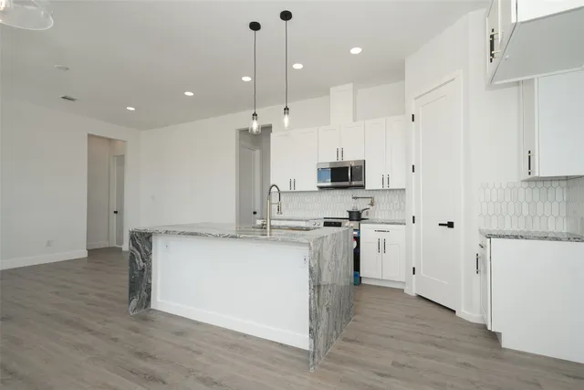 a kitchen with stainless steel appliances kitchen island granite countertop a stove a sink a refrigerator and white cabinets with wooden floor