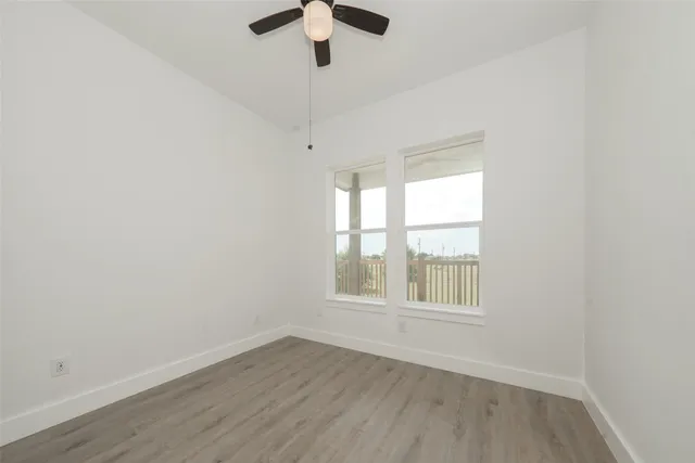 an empty room with wooden floor fan and windows