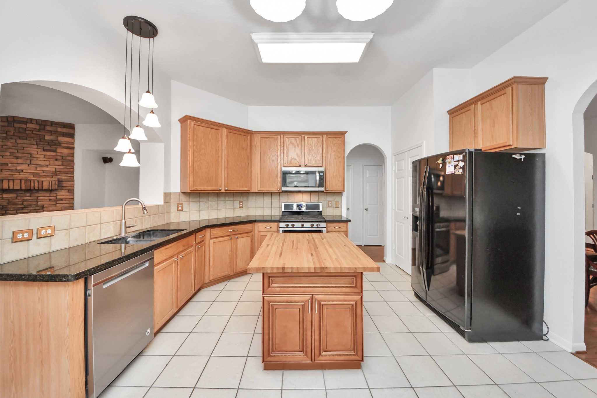 5622 Pineaster Pointe Lane Spring, TX 77379 - Photo 13 of 40 Spacious kitchen featuring wood cabinetry, dark countertops, stainless steel sink, tile backsplash, and a central island with a wood-finish top
