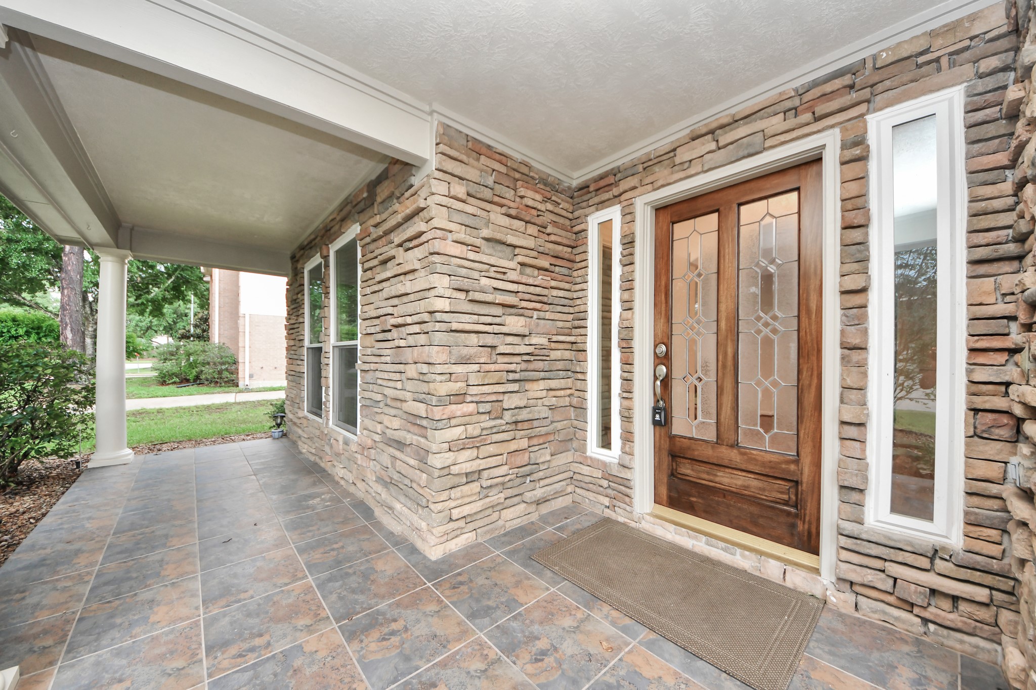 5622 Pineaster Pointe Lane Spring, TX 77379 - Photo 4 of 40 Stacked stone exterior with a covered porch featuring a decorative wood-panel entry door, leaded glass sidelights, and large format floor tiles