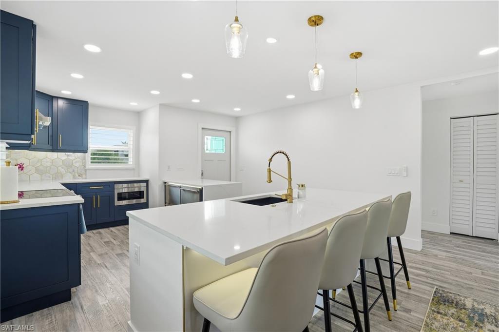 270 Dundee Road Fort Myers Beach, FL 33931 - Photo 13 of 48 Kitchen featuring blue cabinetry, a kitchen island with sink, pendant lighting, recessed lighting, and decorative backsplash - Virtually Edited Image