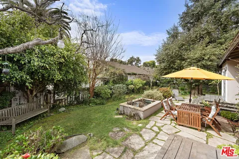 a view of a patio with table and chairs under an umbrella with large trees
