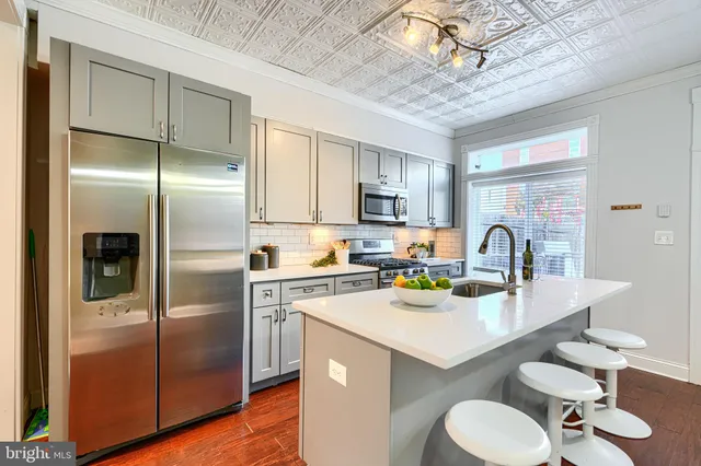 a kitchen with stainless steel appliances a refrigerator a sink a stove and chairs with wooden floor