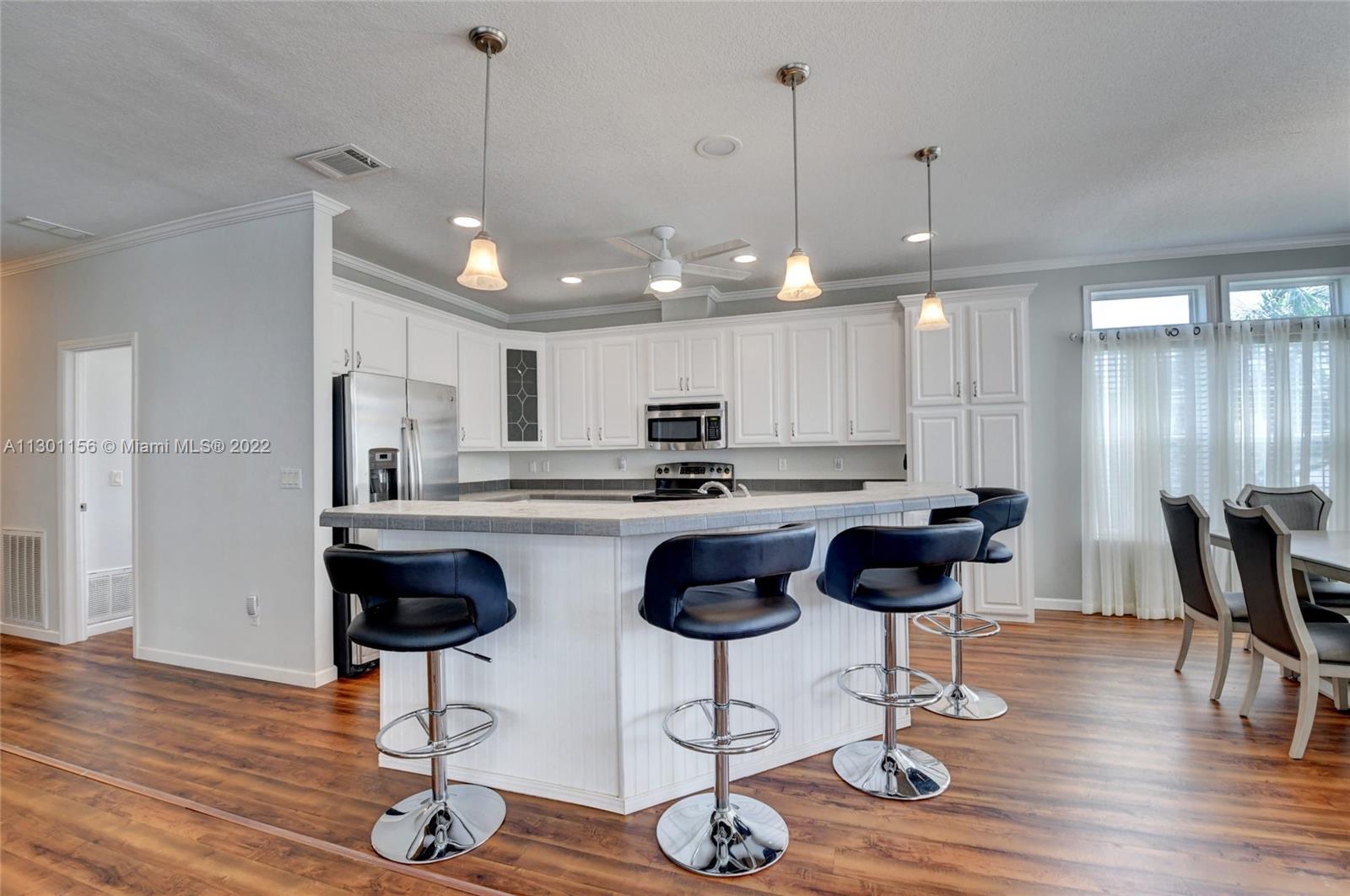 8293 East Club Road Boca Raton, FL 33433 - Photo 8 of 41 a kitchen with stainless steel appliances kitchen island granite countertop a refrigerator a stove a kitchen island with chairs and wooden floor
