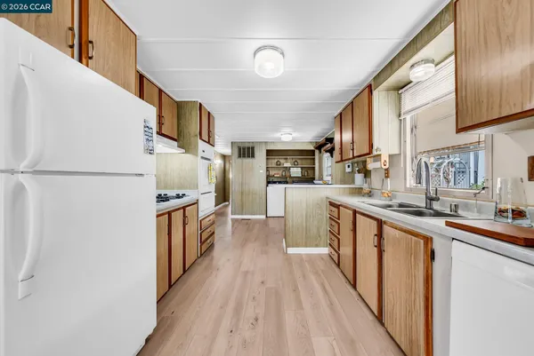 a kitchen with stainless steel appliances granite countertop a refrigerator a sink dishwasher a stove and white countertops with wooden floor