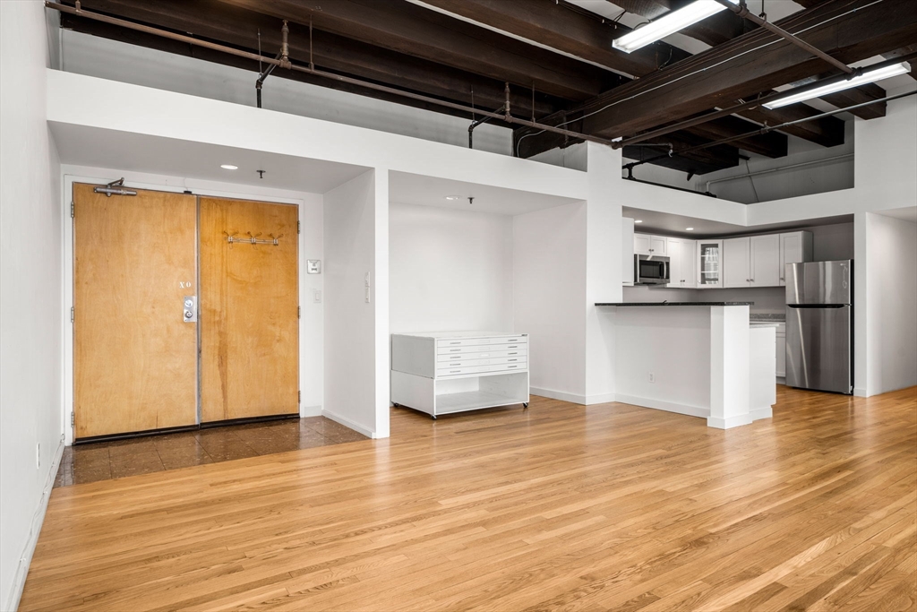 259 A Street, Unit 21 Boston, MA 02210 - Photo 4 of 18 a view of a refrigerator in kitchen and an empty room with wooden floor