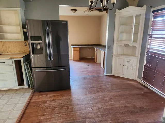 a view of a refrigerator in kitchen and an empty room with wooden floor