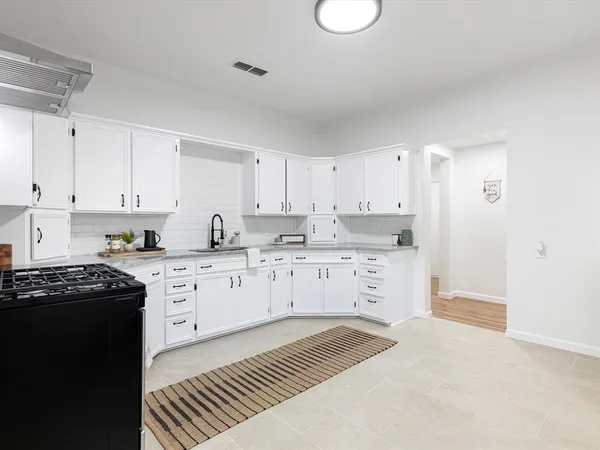 a kitchen with stainless steel appliances granite countertop a stove a sink dishwasher and white cabinets with wooden floor