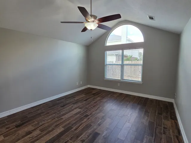 an empty room with wooden floor chandelier fan and windows