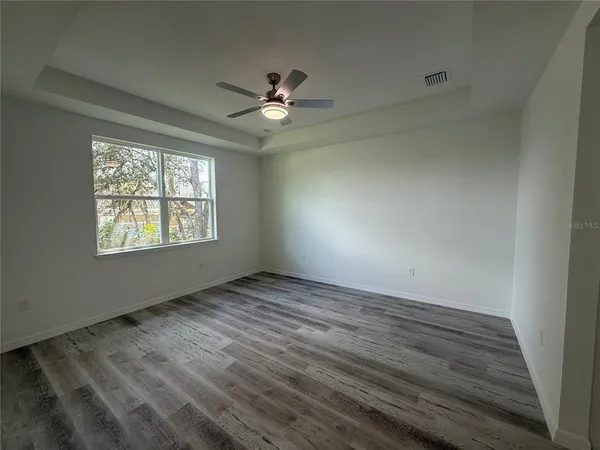 an empty room with wooden floor fan and windows