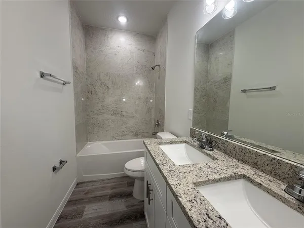 a bathroom with a granite countertop bathtub sink vanity mirror and toilet