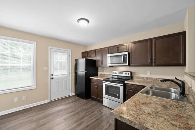 a kitchen with stainless steel appliances granite countertop a stove a sink dishwasher a refrigerator and a microwave oven with wooden floor