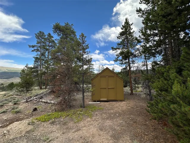 a view of a barn in a yard with plants and large trees