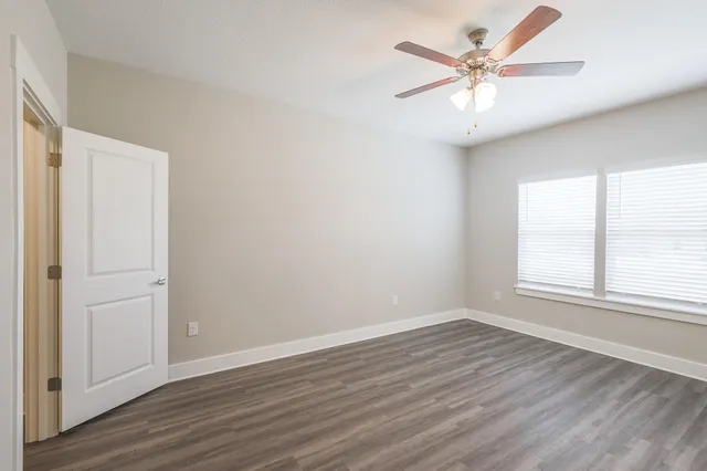 an empty room with wooden floor ceiling fan and windows