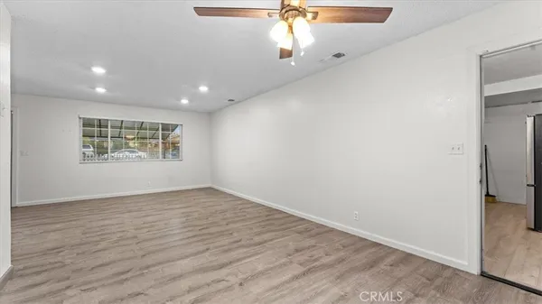 an empty room with wooden floor chandelier fan and windows