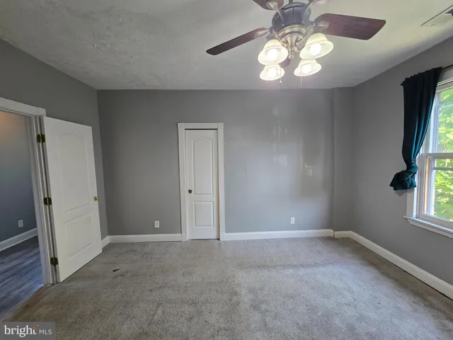 a view of an empty room with window and chandelier fan