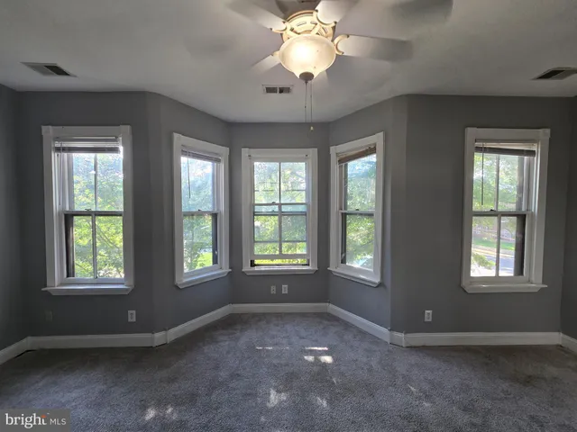 an empty room with chandelier fan and windows