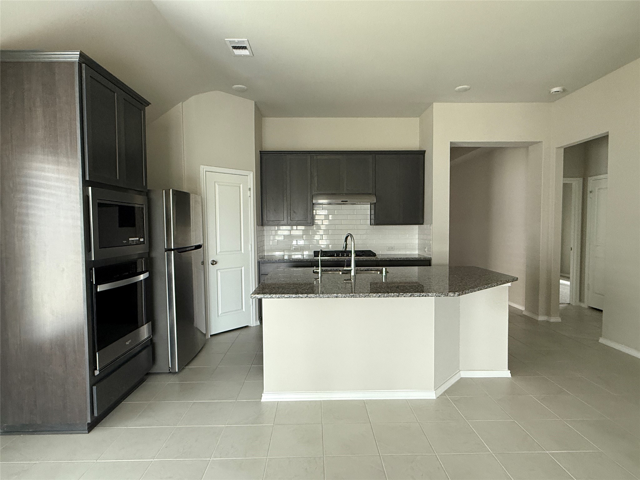31961 Retama Rnch Drive Spring, TX 77386 - Photo 11 of 25 Modern kitchen with stainless steel appliances, a granite countertop island, and dark cabinetry. The space features a sleek tile floor and neutral walls, creating a clean and inviting atmosphere.