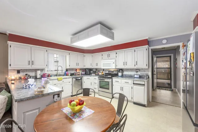 a kitchen with stainless steel appliances a dining table chairs sink and cabinets