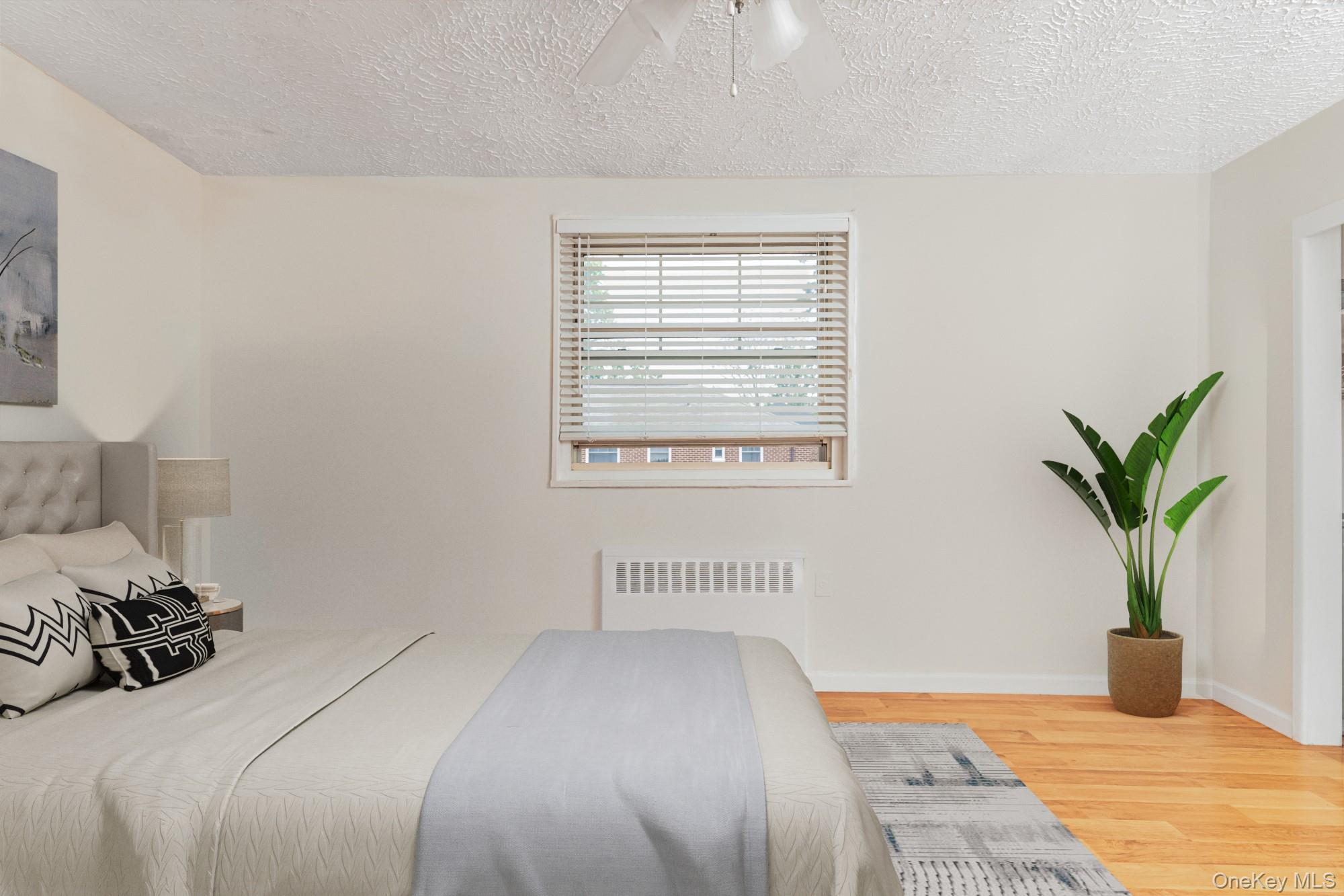 61-15 251st Street, Unit 1100 Queens, NY 11362 - Photo 2 of 17 STAGED: Bedroom with wood finished floors, radiator, a textured ceiling, and a ceiling fan