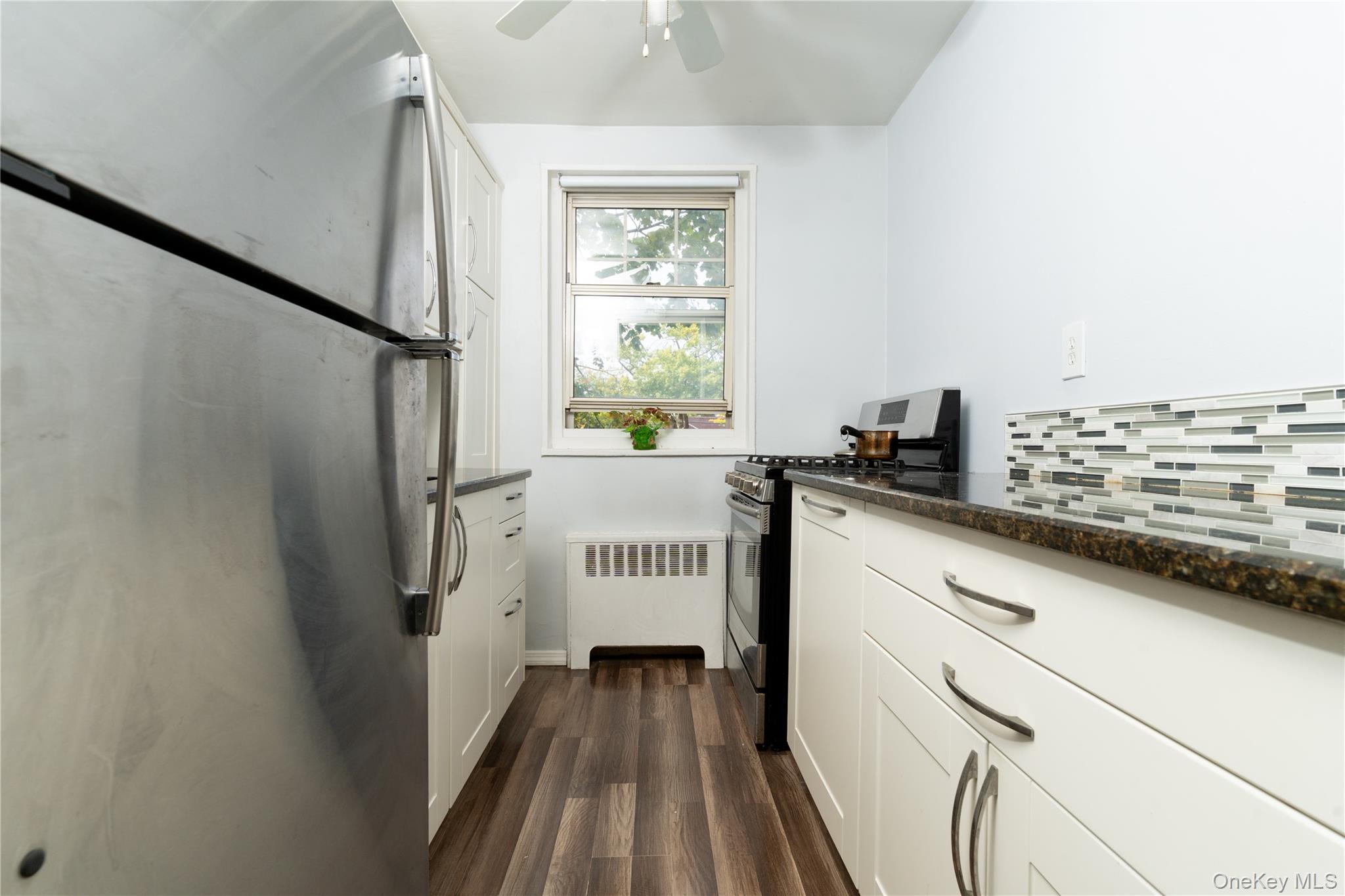61-15 251st Street, Unit 1100 Queens, NY 11362 - Photo 5 of 17 Kitchen featuring stainless steel appliances, white cabinets, radiator, dark wood finished floors, and dark stone countertops