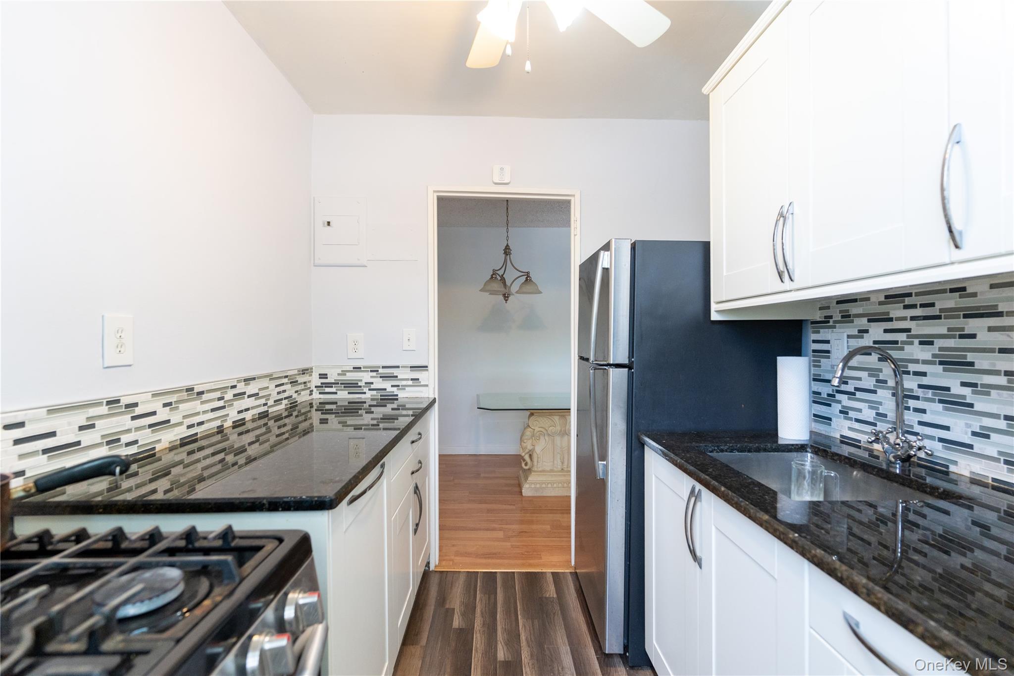 61-15 251st Street, Unit 1100 Queens, NY 11362 - Photo 7 of 17 Kitchen featuring dark stone counters, tasteful backsplash, dark wood-style floors, and white cabinets