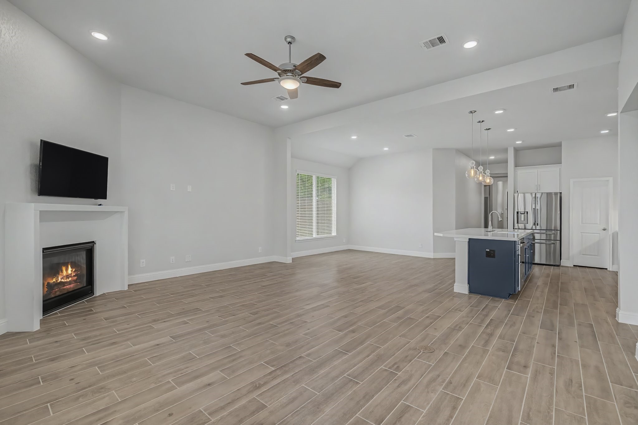 21339 Sierra Point Lane Porter, TX 77365 - Photo 13 of 36 This spacious open-concept living area features modern wood-look tile flooring, a cozy fireplace, and a ceiling fan. It flows seamlessly into a bright kitchen with a large island, pendant lighting, and stainless steel appliances, perfect for entertaining.