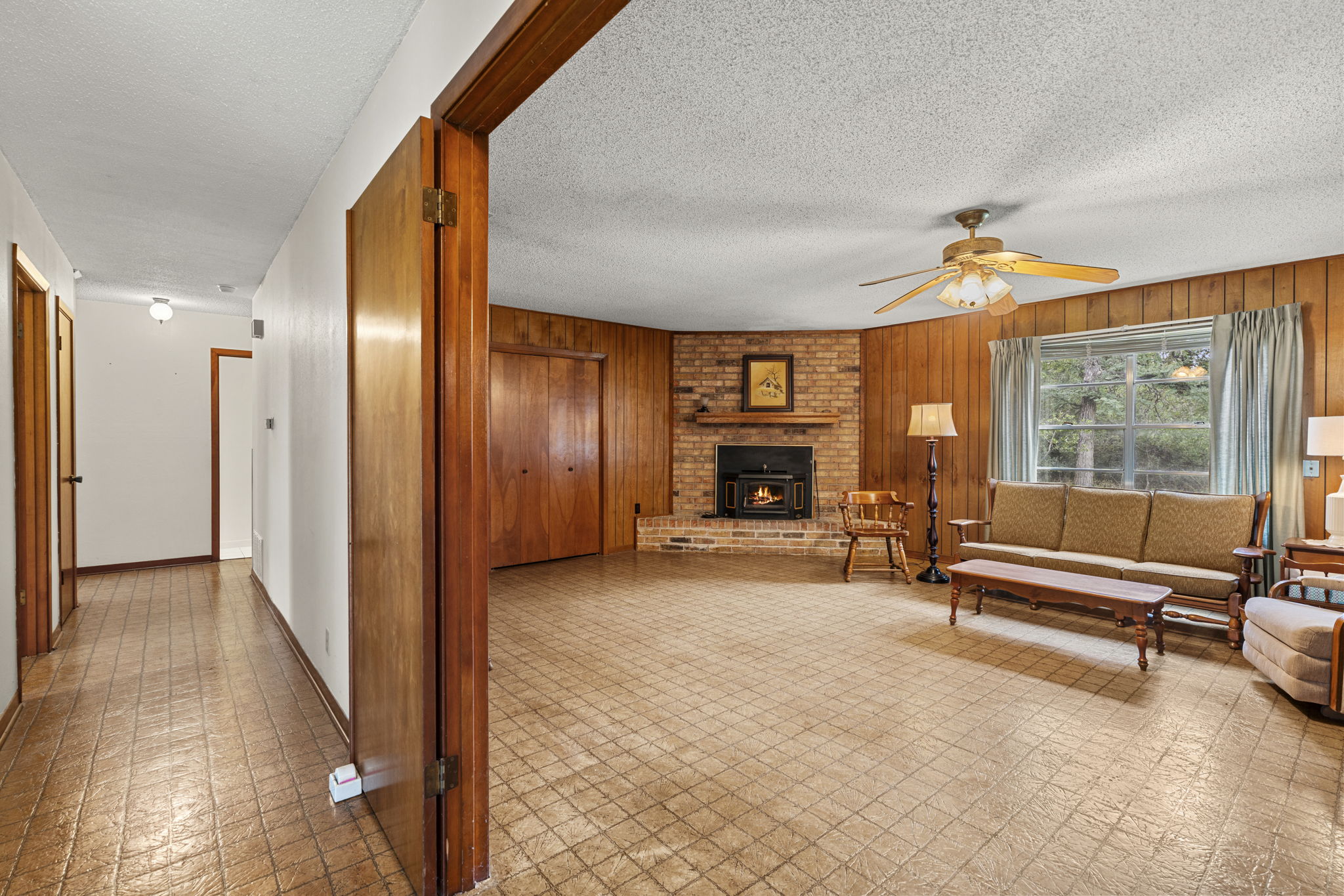 3511 Wyldwood Road Austin, TX 78739 - Photo 12 of 40 Living room with ceiling fan, wood walls, a brick fireplace, a textured ceiling, and tile patterned floors