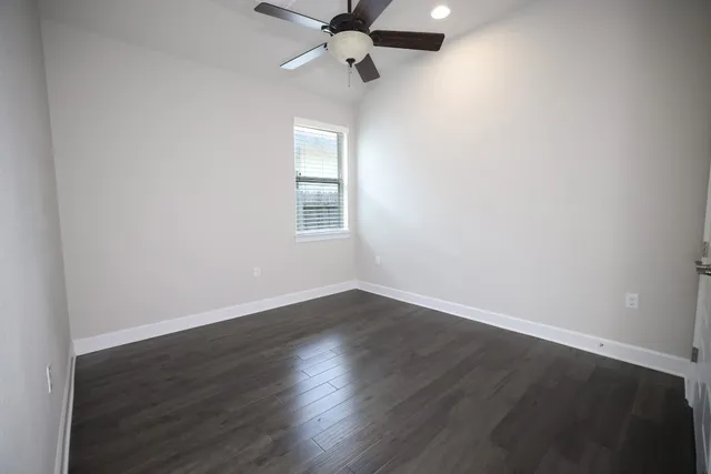 an empty room with wooden floor ceiling fan and windows