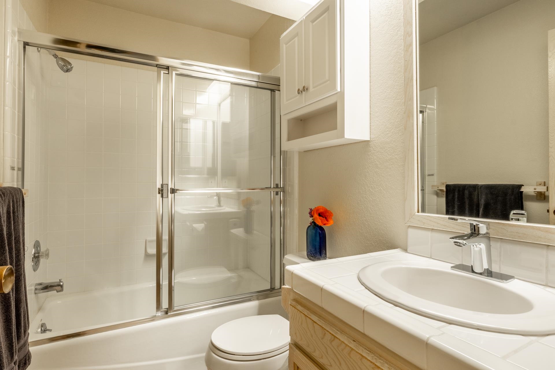 609 Golden Creek Road, Unit 609 Mammoth Lakes, CA 93546 - Photo 17 of 42 Bathroom featuring a built-in tub with a sliding glass enclosure, white tiled walls, a vanity with a tile countertop, an integrated sink, and an overhead mirrored cabinet