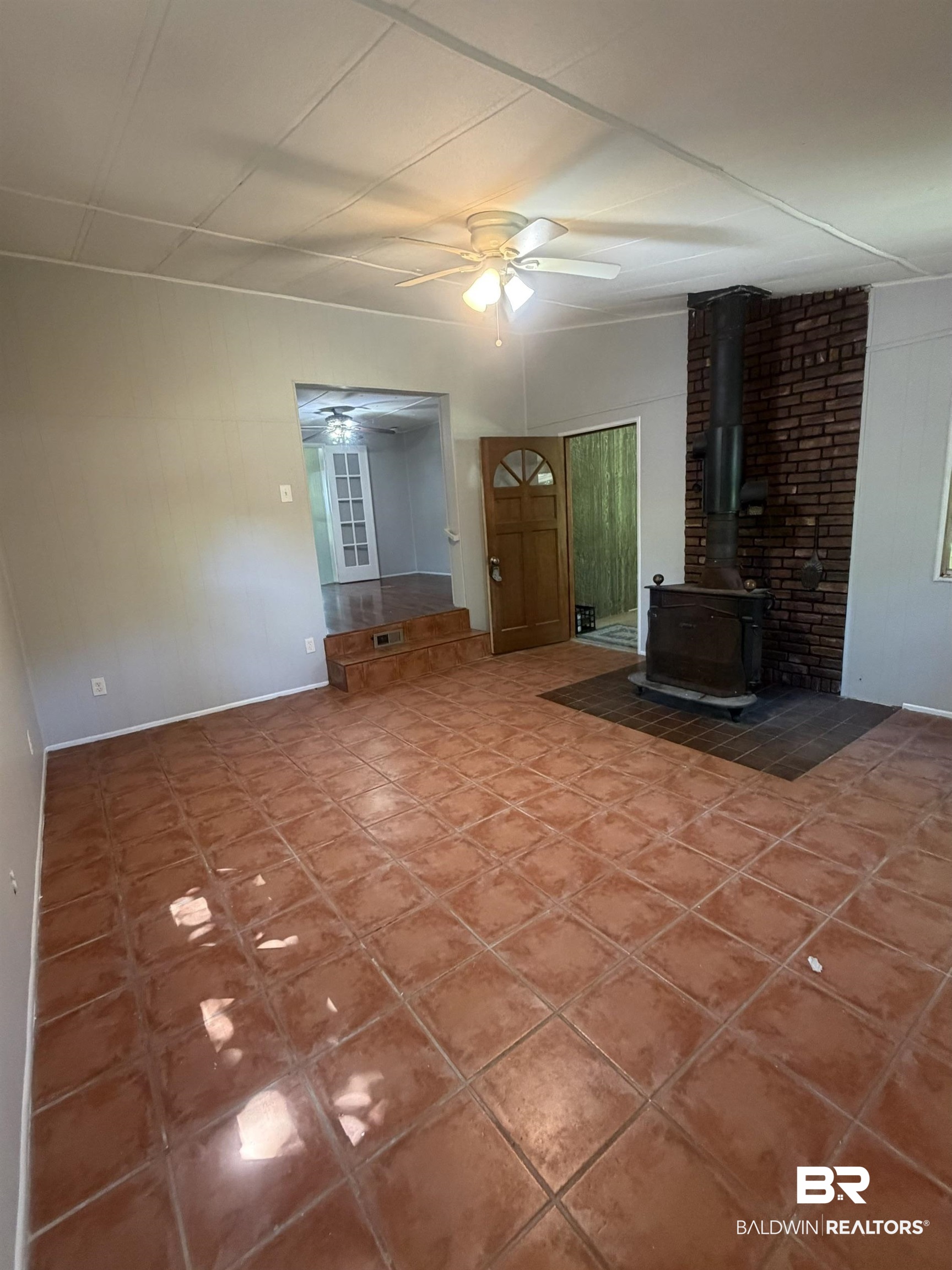 1354 Caney Loop Lillian, AL 36549 - Photo 6 of 45 Spacious room featuring terra cotta tile flooring, a brick accent wall with a wood stove, and a ceiling fan