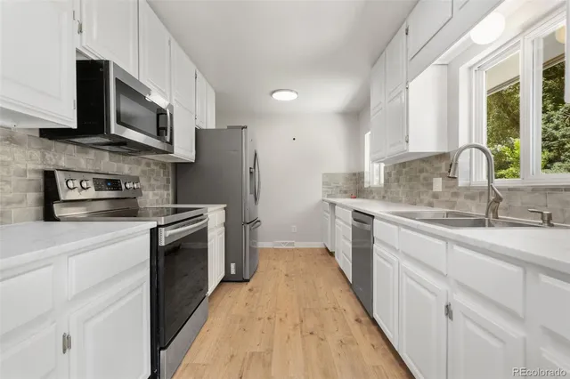 a kitchen with stainless steel appliances granite countertop a sink a stove top oven a refrigerator with grey cabinets and wooden floor