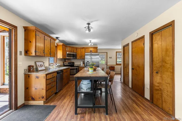 a kitchen with stainless steel appliances granite countertop a stove a refrigerator a kitchen island a table and chairs in it