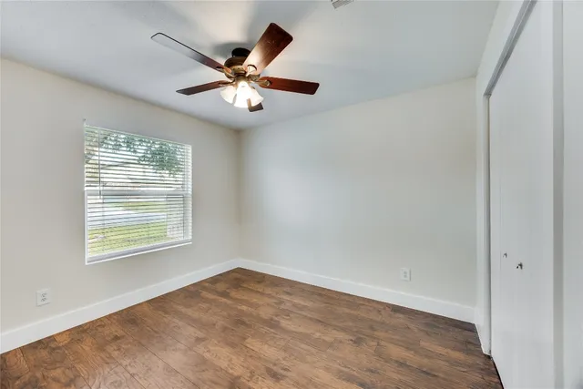an empty room with wooden floor fan and windows