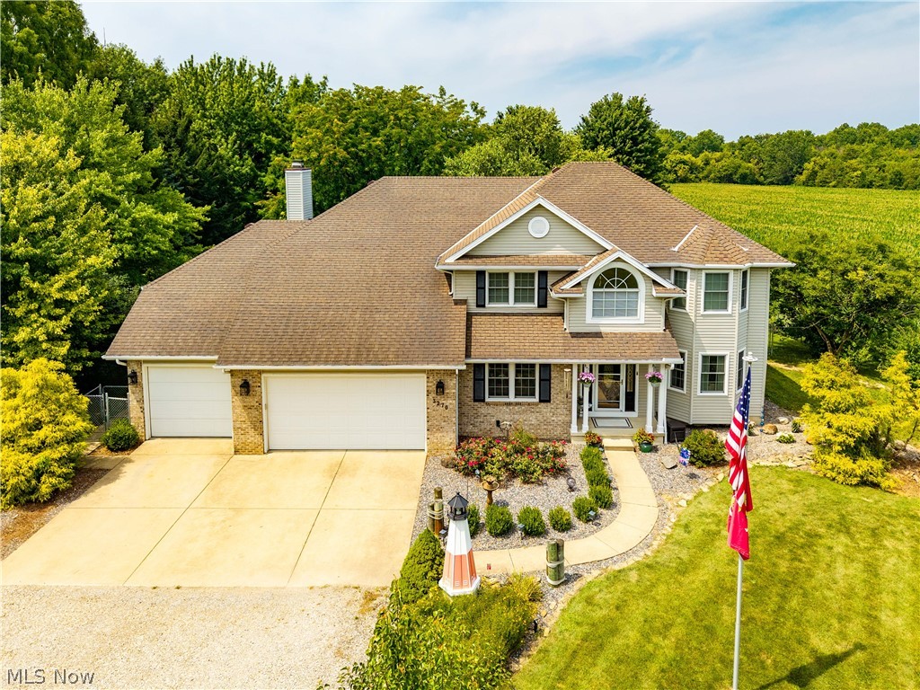 Two-story residence featuring a 4-car garage, stone and vinyl siding exterior, front entry with columns, and a paved driveway