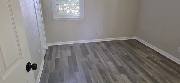 a view of an empty room with wooden floor and a window