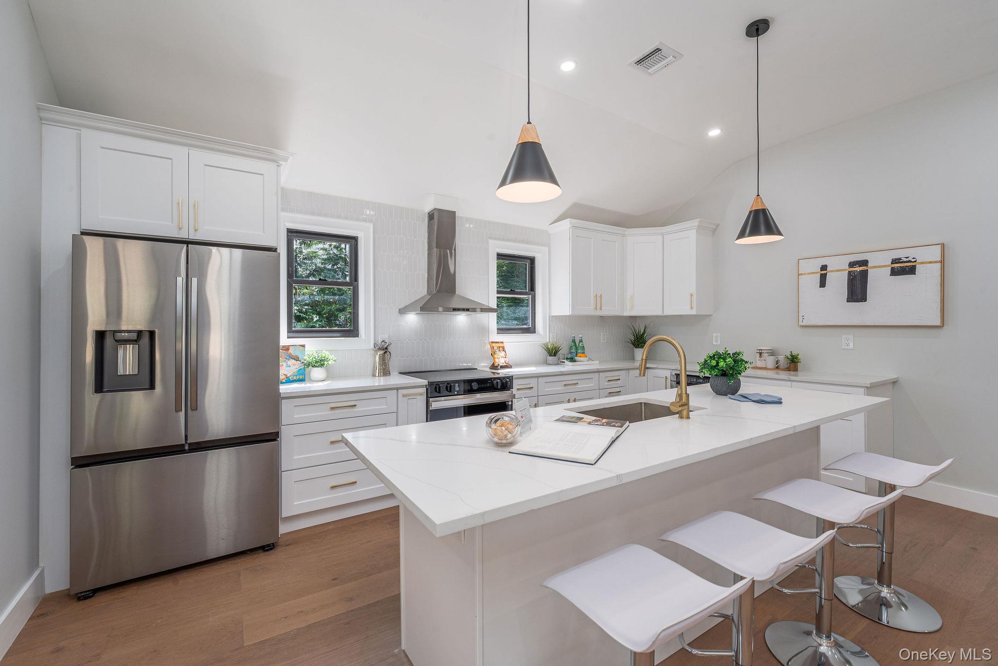 3420 Rocky Point Road East Marion, NY 11939 - Photo 9 of 34 Kitchen with appliances with stainless steel finishes, light wood-style floors, wall chimney range hood, white cabinets, and vaulted ceiling