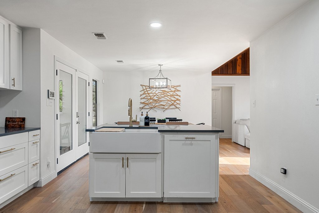 201 Raincloud Road Wimberley, TX 78676 - Photo 15 of 40 Kitchen with an island with sink, white cabinetry, dark countertops, light wood-style flooring, and hanging lights