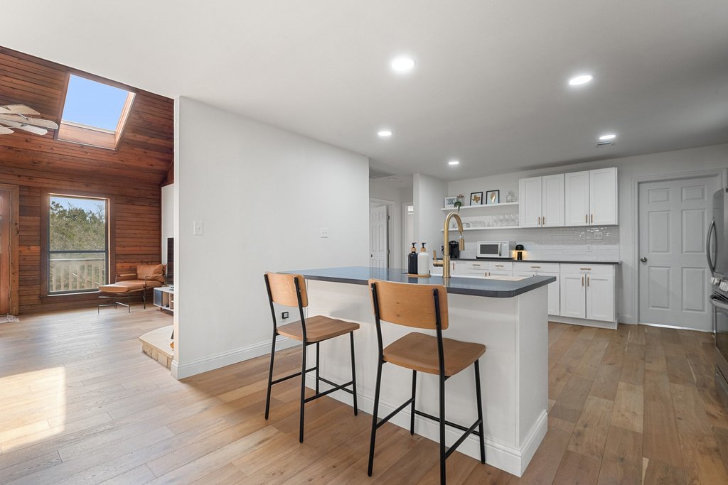 201 Raincloud Road Wimberley, TX 78676 - Photo 16 of 40 Kitchen with white cabinetry, open shelves, a breakfast bar, light wood-type flooring, and wood walls