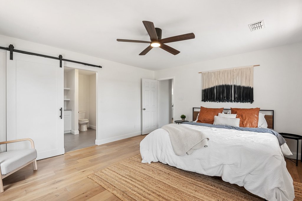201 Raincloud Road Wimberley, TX 78676 - Photo 20 of 40 Bedroom with a barn door, light wood-type flooring, ceiling fan, and connected bathroom