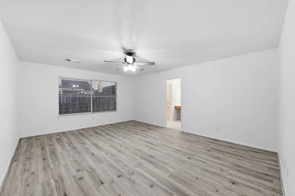 a view of an empty room with wooden floor and fan