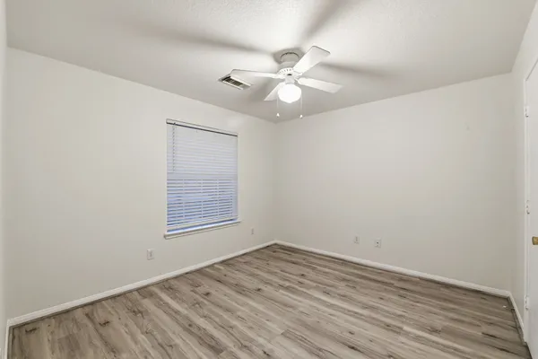 an empty room with wooden floor fan and windows