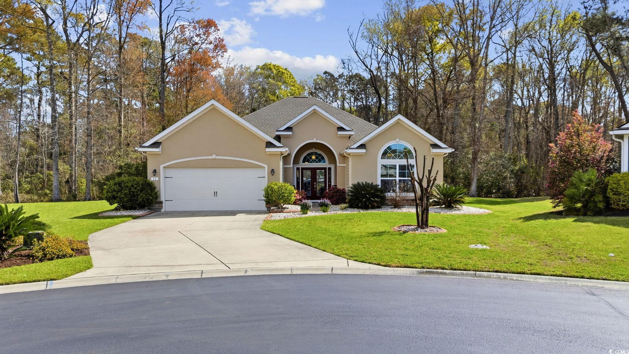 View of front facade featuring stucco siding, a front lawn, french doors, concrete driveway, and an attached garage