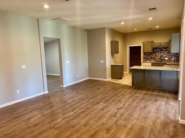 an empty room with kitchen view and wooden floor