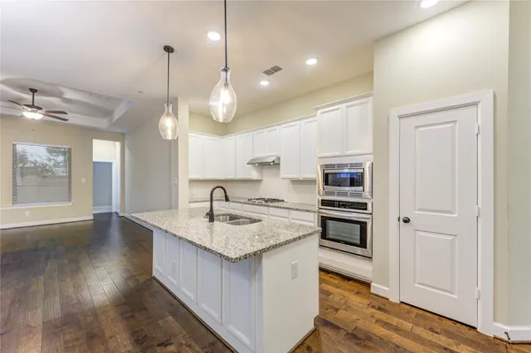 a view of an empty room and a kitchen view with wooden floor