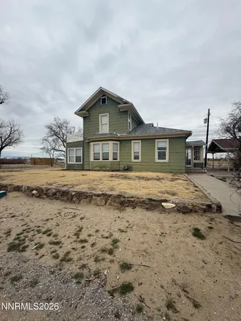 a front view of a house with a dirt yard and a large tree