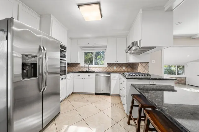 a kitchen with granite countertop white cabinets appliances and a window