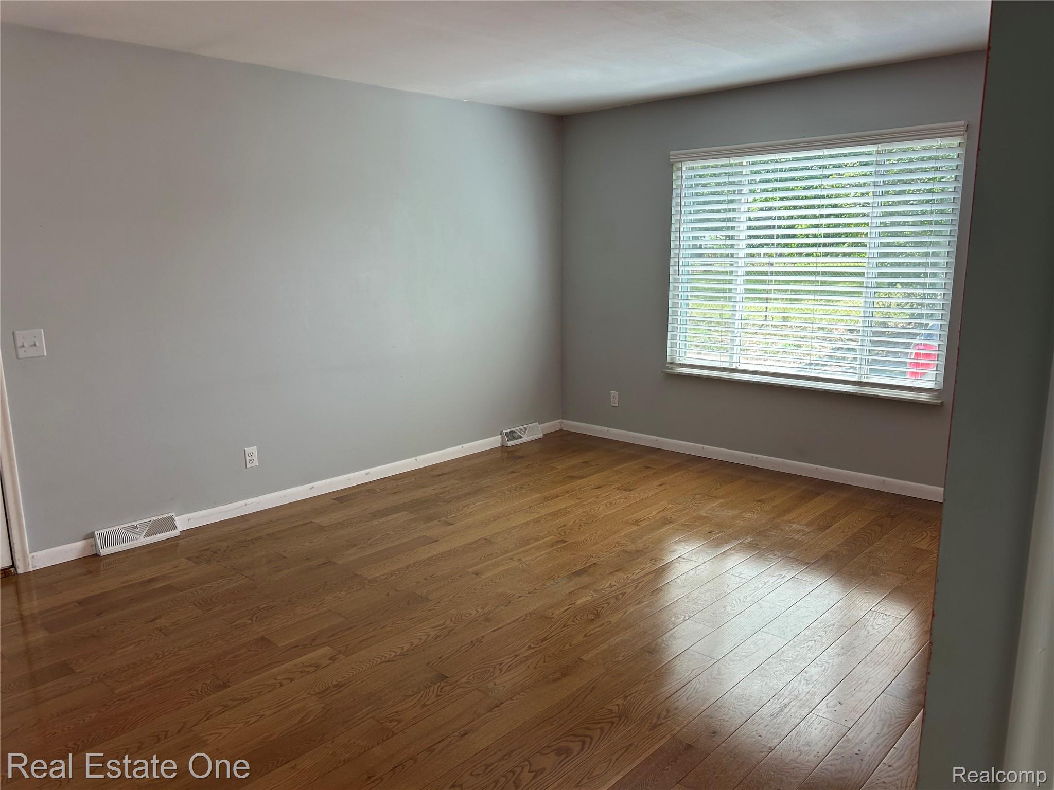 2659 Benstein Road Commerce Township, MI 48382 - Photo 12 of 26 Spacious room featuring wood-finish flooring, light gray wall paint, white trim, and a large window with horizontal blinds